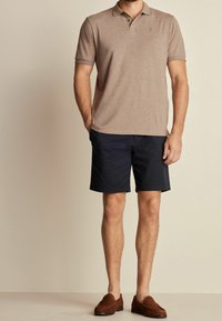 Hnědá polo tričko s krátkým rukávem, námořnické šortky a hnědé slip-on boty. Jednoduchý design a klasický střih. Minimální branding na tričku.