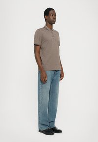 Brun mönstrad polo skjorta med korta ärmar, ihop med ljusblå raka jeans och svarta skor. Enkel och avslappnad design.