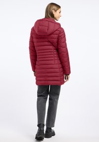 Rode gewatteerde jas met een capuchon, met een gestikt ontwerp en verticale naden. Gecombineerd met grijze broeken en zwarte laarzen.