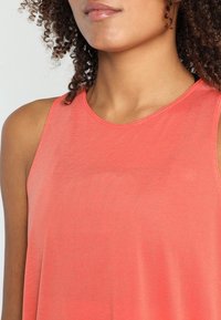Top senza maniche color corallo con scollatura rotonda e tessuto leggero e strutturato, caratterizzato da sottili righe orizzontali e una vestibilità morbida.