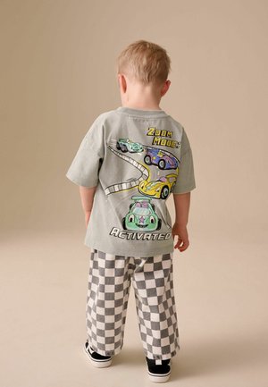 Graues T-Shirt mit Cartoon-Auto-Grafiken und Text auf der Rückseite, kombiniert mit schwarz-weiß karierten Hosen, getragen mit schwarzen Turnschuhen.