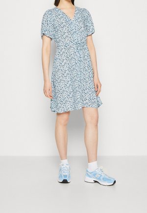 Abito floreale blu con maniche corte a sbuffo, scollatura a V e vita arricciata. Indossato con sneaker azzurre.