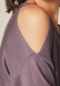 Purple, metallic knit top featuring shoulder cutouts and a soft texture. The fabric has a slight shimmer and a relaxed fit design.