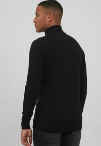 Schwarzer Rollkragenpullover aus geripptem Strickstoff. Mit langen Ärmeln und einer taillierten Silhouette. Keine sichtbaren Muster oder Akzente.