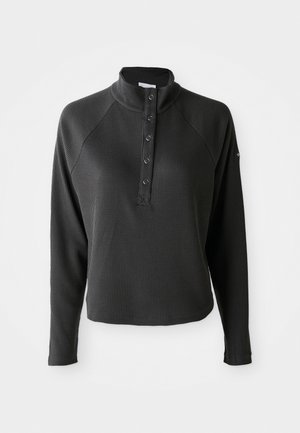 Pullover lungo a manica con colletto alto in maglia waffle nera, con cinque bottoni a pressione sul davanti, esposto su uno sfondo bianco.