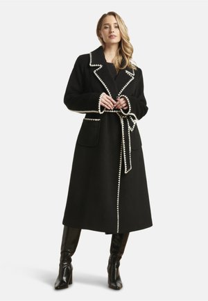 Black wool coat with contrasting white trim, large collar, two front pockets, and a matching belt; mid-length design, soft texture.