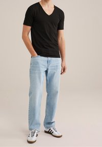 T-shirt nera in cotone con scollo a V abbinata a jeans di denim azzurro chiaro. Sneakers bianche con strisce nere completano il look. Ensemble semplice e casual.