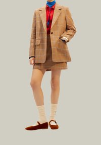 Hnědý kostkovaný blazer s odpovídající sukní, červená košile, modrý rolák, béžové žebrované ponožky a hnědé sametové baleríny s detailem pásku.