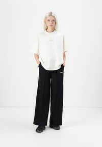 Oversized white cotton t-shirt with short sleeves and subtle logo. Paired with wide-leg black pants featuring white lettering. Black sneakers.