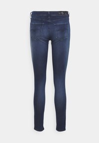 Jeans ajustados en denim azul oscuro. Presentan una cintura de altura media, dos bolsillos traseros con costuras curvas y una textura suave.