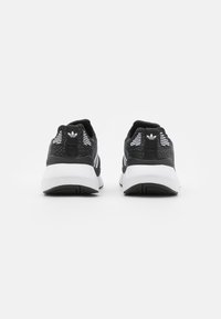 Scarpe sportive nere con parte superiore in tessuto testurizzato, strisce bianche e suola bianca solida. Presentano una linguetta posteriore e dettagli con logo.