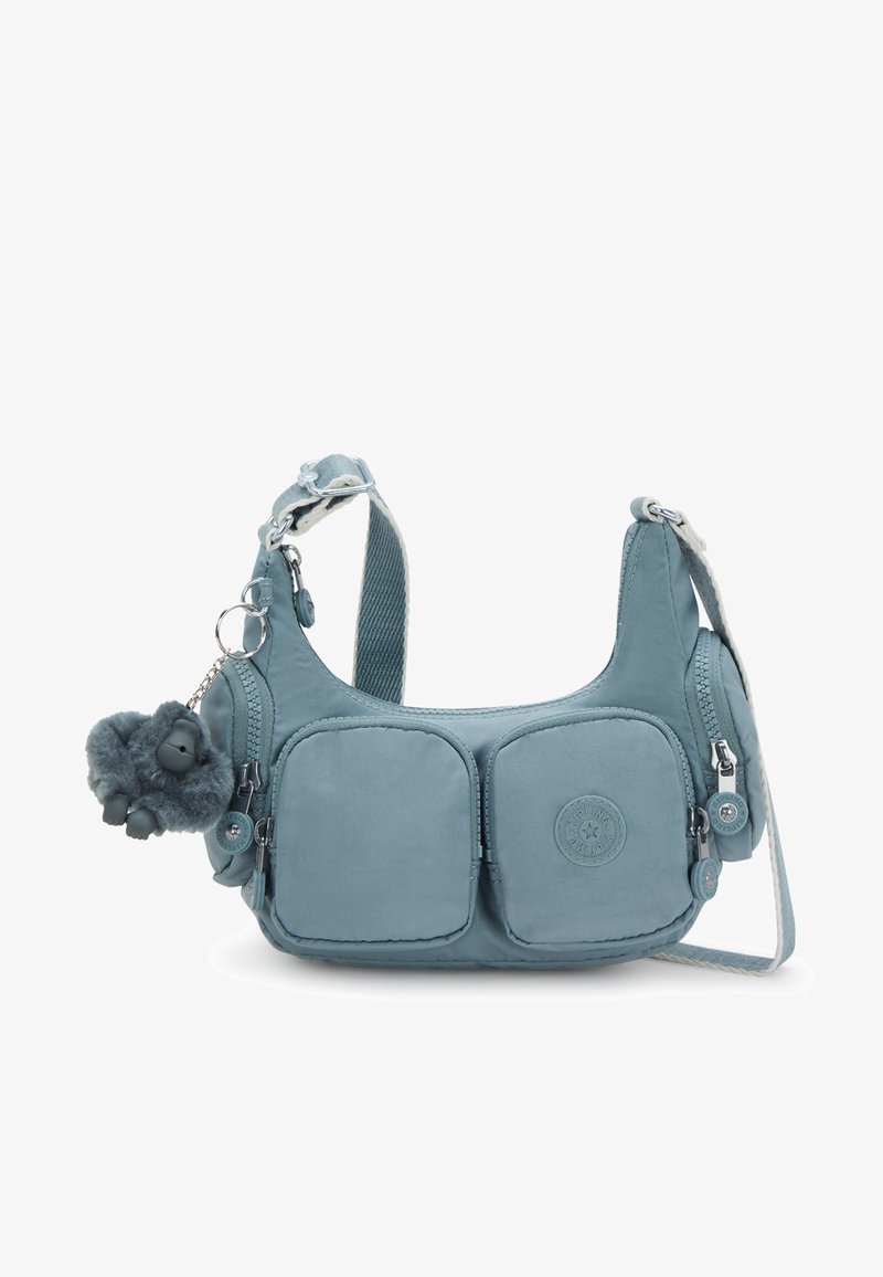 Blå tygaxelväska med två framfickor, silverdetaljer och en lurvig apcharms. Har en justerbar rem.