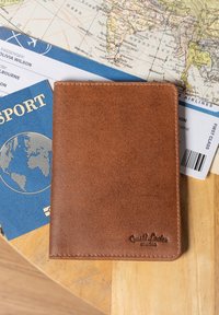 Porte-passeport en cuir marron sur une table en bois avec un passeport bleu, un billet d'avion et une carte du monde vintage en dessous.