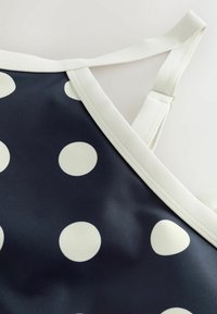Tissu bleu marine avec de grands pois blancs, bordure blanche et une sangle d'épaule blanche réglable.