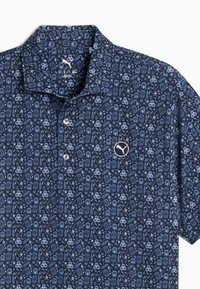 Donkerblauwe polo shirt met een knoopsluiting kraag en een ingewikkeld lichtblauw grafisch patroon van verschillende objecten, met een witte Puma-logo op de borst.