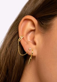 Orecchini d'oro con una catena che collega un cerchio con un accento in cristallo e un ciondolo a punta, che mostrano un design elegante e moderno.