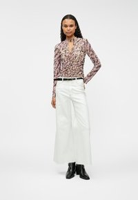 Koszula z długim rękawem w różowo-czarny abstrakcyjny wzór z dekoltem w kształcie łezki. Połączona z białymi dżinsami o szerokich nogawkach i czarnymi botkami na kostkę.