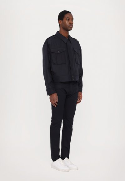 Tengerészeti cropped dzseki, két elülső zsebbel, gombos záródással és galléros nyakkal, slim fit fekete nadrággal és fehér sportcipővel párosítva.
