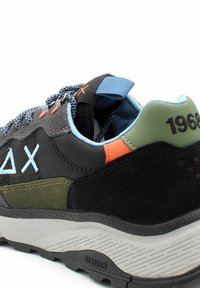 Sneaker nero e grigio con una parte superiore testurizzata, accenti blu chiaro, evidenziature arancioni e verdi, e una suola in gomma grigia. Include una linguetta imbottita.