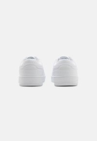 Białe sneakersy z gładką syntetyczną cholewką, wyściełanym kołnierzem i teksturowaną gumową podeszwą, z subtelnym logo na pięcie.