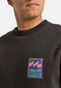 Sudadera negra con cuello acanalado, que presenta un logo bordado colorido en rosa, azul y verde en el lado izquierdo del pecho.