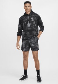 Juodas ir pilkas tye-dye tipo gobtuvas su priekinėmis kišenėmis, derinamas su atitinkamomis šortais. Medžiaga atrodo minkšta; išvaizdą užbaigia sportiniai bateliai ir kojinės.