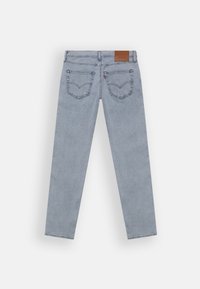 Ljusblå denimjeans liggande platt, som visar baksidan med två påsydda fickor och en brun läderlogg på midjebandet.