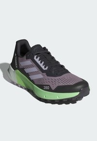 Scarpa da trail nera e verde con tomaia texture, dettagli grigi e suola spessa progettata per la presa. Presenta tre strisce bold sul lato.