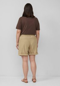 Braunes kurzärmliges Hemd und beiges Shorts mit umgeschlagenem Saum. Die Shorts haben einen elastischen Bund und Gesäßtaschen und bestehen aus weichem Stoff.