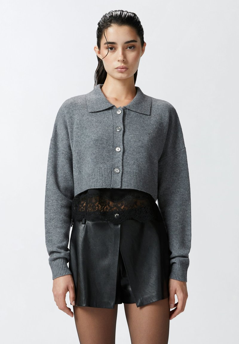 Maglione grigio corto con colletto e chiusura a cinque bottoni. Abbinato a pantaloni corti in ecopelle nera con rifinitura in pizzo.