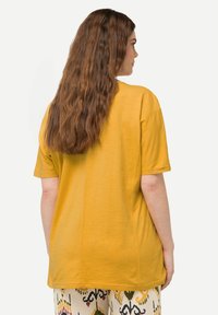 T-shirt colore giallo senape con maniche corte, vestibilità rilassata, texture liscia e un sottile dettaglio cucito sul retro. Abbina a pantaloni fantasia.