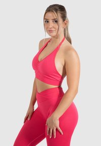 Felroze sport-beha met een geplooid front en halternek, gecombineerd met hoge taille leggings. Soepele textuur en aansluitend ontwerp.