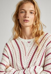 Trikotāžas džemperis krēmkrāsā ar izteiktiem rozā un bordo vertikāliem un diagonāliem svītrām. Iezīmēts ar atvērtu dzijas dizainu un ribotiem apkakles galiem.