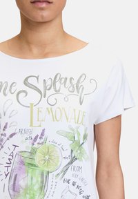 Biała koszulka z krótkim rękawem z kolorową ilustracją lemoniady z zielonymi i purpurowymi akcentami oraz zabawną typografią i grafiką.