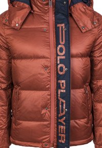 Giubbotto imbottito arancione bruciato con finitura lucida, con un pannello frontale blu navy che presenta la scritta "POLO PLAYER" e diversi bottoni a pressione.