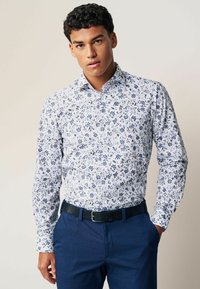 Cămașă albă cu mâneci lungi, cu model floral albastru, guler cu nasturi. Purtați cu pantaloni de costum albaștri închisi și o curea neagră.