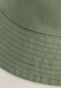 Groene katoen bucket hat met een textuur, voorzien van gestikte lijnen rond de rand en een ronde kroon voor een klassieke uitstraling.