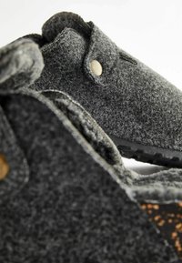 Szare buty z miękkiego materiału o zaokrąglonym kształcie, z detalem w postaci złotego guzika. Podeszwa jest wzorowana dla lepszej przyczepności.