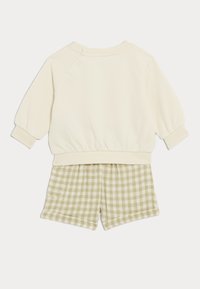 Felpa crema con maniche a sbuffo e polsini a coste, abbinata a pantaloni corti verde a quadri. Tessuto morbido, design casual, con tasche laterali.