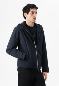 Námořnická modrá bunda na zip s kapucí, má dlouhé rukávy a bílomodrý akcent na zipu. Hladká textura a lehký design.