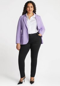 Blazer lavande, chemise blanche avec plis verticaux, pantalon slim noir et escarpins noirs à bout pointu. Tissu lisse et coupe ajustée.