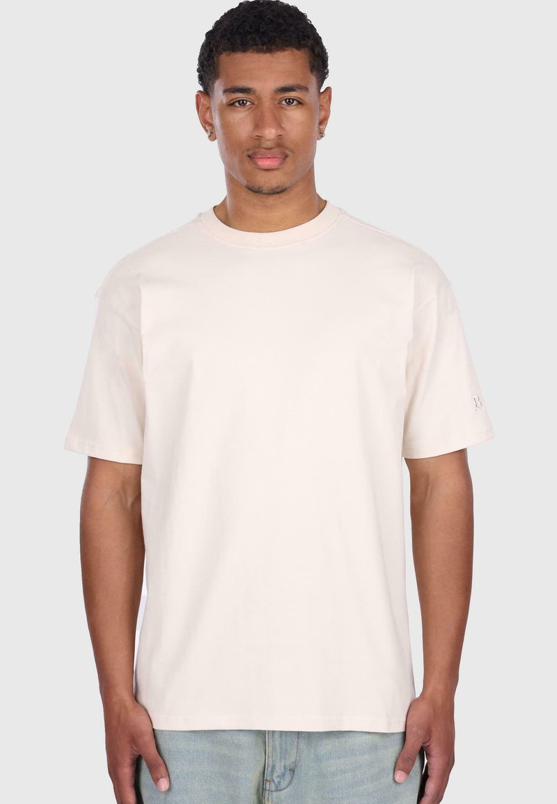 Hellbeige Baumwoll-T-Shirt mit Rundhalsausschnitt, kurzen Ärmeln und lockerer Passform. Dezente Markenkennzeichnung auf dem linken Ärmel.