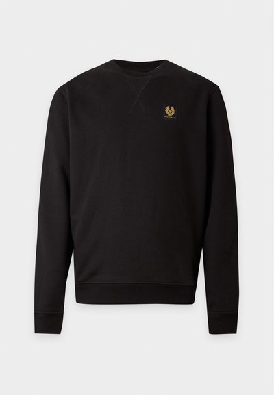 Sweat-shirt noir uni à manches longues et col rond, avec poignets et ourlet côtelés, arborant un petit logo patch doré et noir sur la poitrine gauche.