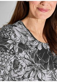 Bloemrijke top met een zwarte achtergrond en witte lijntekeningen van bloemen. Het heeft een ronde halslijn en een gestructureerde stof.