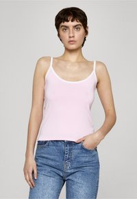Svetloružový tielko s tenkými bielymi ramienkami a zaobleným výstrihom, s hladkou textúrou. Kombinované s modrými vysokým pásom džínsami.