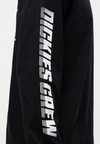 Μαύρο μακρυμάνικο βαμβακερό T-shirt με άσπρο κείμενο «DICKIES CREW» κάθετα κατά μήκος του δεξιού μανικιού σε έντονη, υφή γραμματοσειρά.
