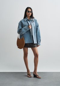 Denim oversized jacket in light blue, worn over a gray top and black mini skirt. Brown shoulder bag and black wedge sandals complement the look.