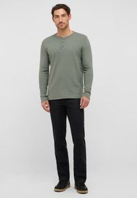 Długi rękaw, oliwkowa bluzka henley z trzema guzikami. Noszona z czarnymi jeansami o prostym kroju i czarnymi trampkami. Gładka faktura.