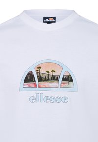 Camiseta blanca con un estampado gráfico colorido de palmeras y canchas de tenis, con el nombre de la marca "ellesse" debajo en azul claro.