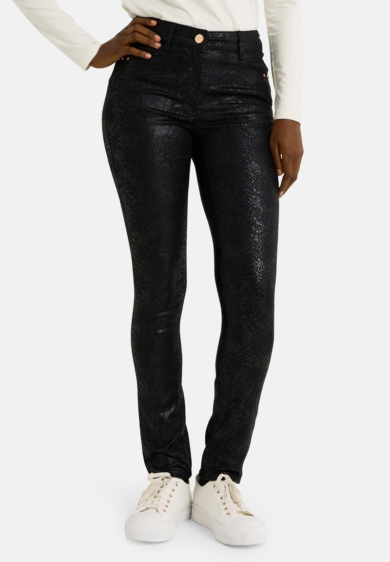 Jean noir taille haute avec une texture de peau de serpent, finition brillante et un bouton en cuivre à la taille. Stylé avec des baskets blanches.